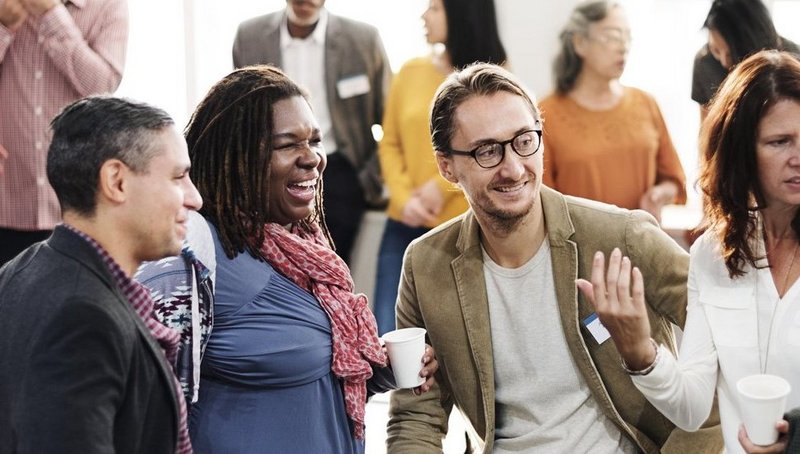 Zwei Männer und drei Frauen unterhalten sich und lachen auf einer Netzwerk-Veranstaltung