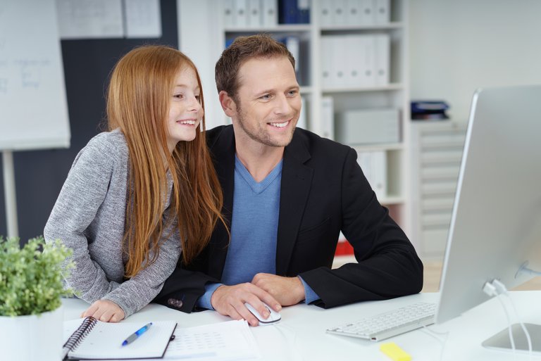 Ein Mann in schwarzem Sakko und ein Mädchen im Grundschulalter mit langen roten Haaren schauen gemeinsam auf einen Bildschirm