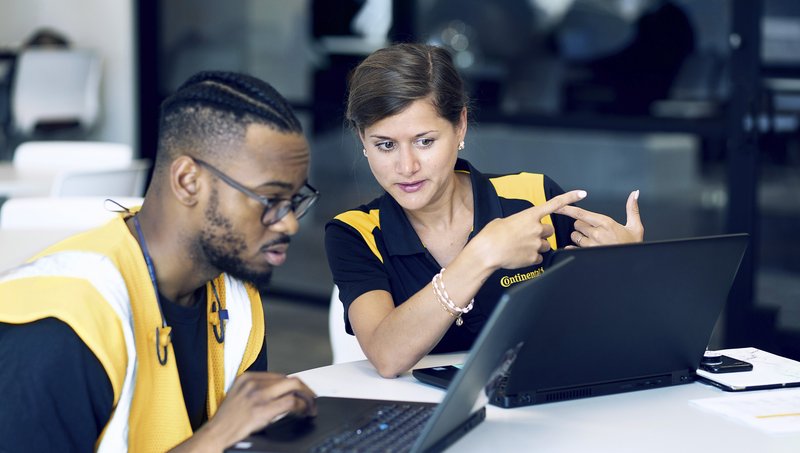 A man and a woman in yellow high-visibility waistcoats look at a screen