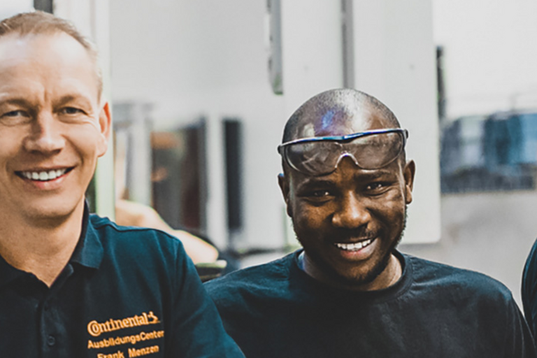 Ein älterer Mann und ein Mann mit Sicherheitsbrille auf der Stirn schauen lächelnd in die Kamera