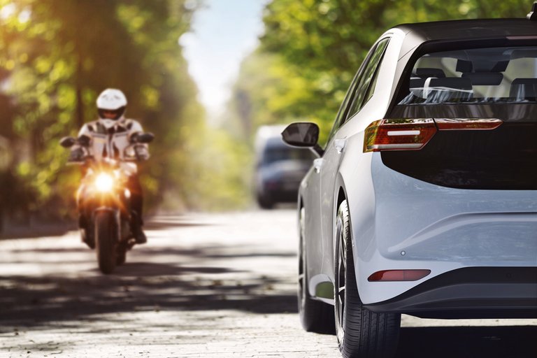Ein Elektroauto fährt an einem Motorradfahrer vorbei