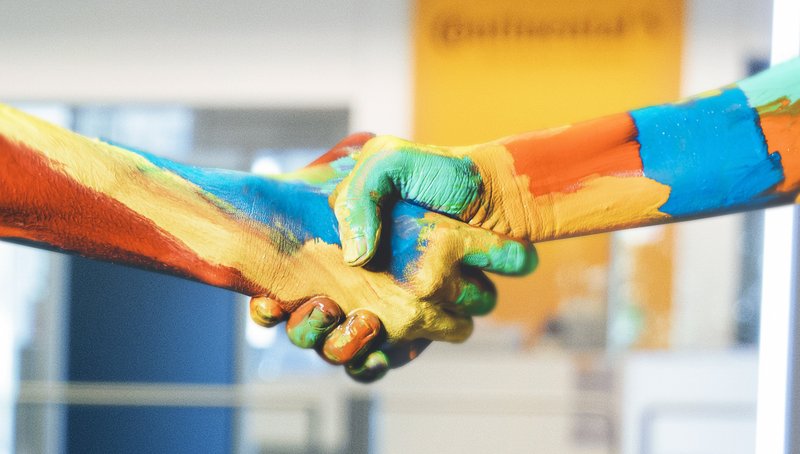 Zwei mit bunten Farben bemalte Hände schütteln sich vor einem unscharfen Hintergrund 