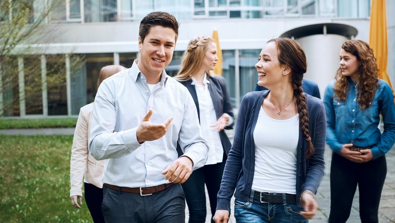 A young man and three young women walk in front of a building and smile