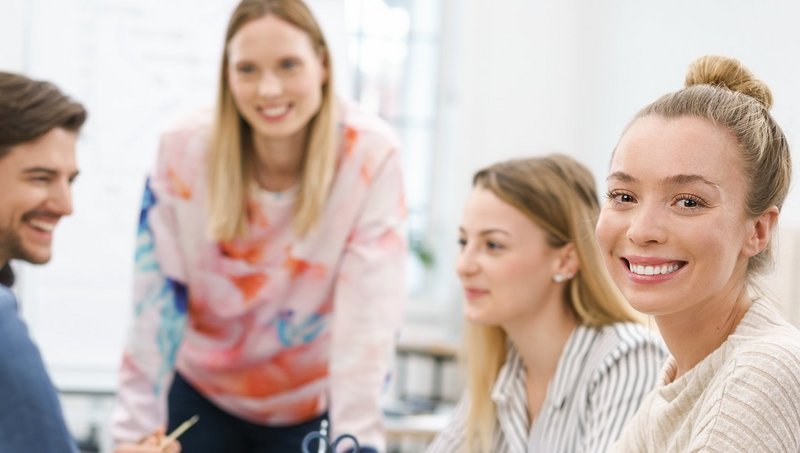 Eine Gruppe von vier jungen Frauen und einem jungen Mann sitzt an einem Tisch und lächelt