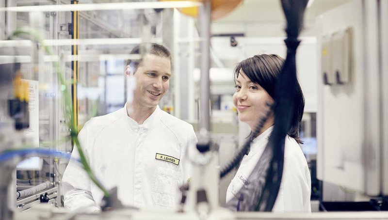 A woman and a man in smocks stand between production machinery