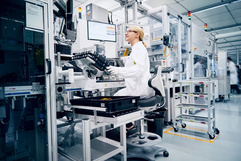 A woman in white coat and gloves controls a technical machine