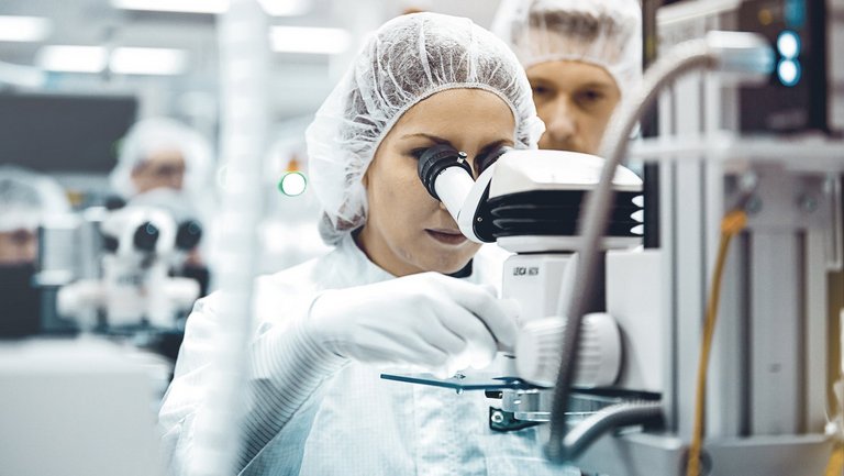A woman looking through a microscope in a sterile laboratory setting