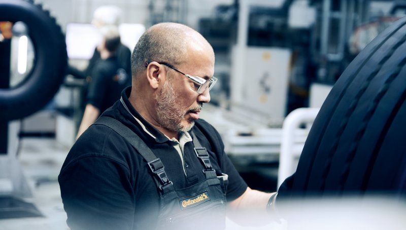 Ein älterer Mann mit Dreitage-Bart in Latzhose prüft einen Reifen