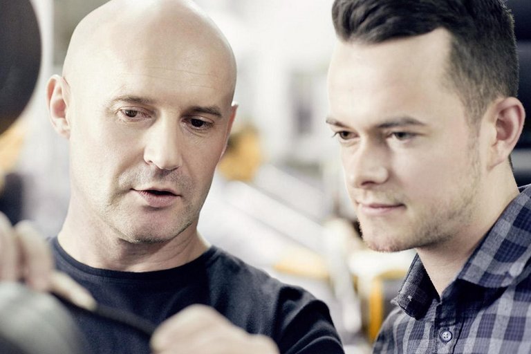 A bald man explains a technical product to a younger man in a check shirt