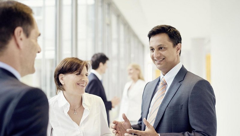 A group of a woman and two men are standing in the foreground discussing about a topic