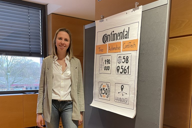 Eine Frau in Jeans, weißer Bluse und beigem Sakko steht in einem Konferenzraum an einem Flipchart