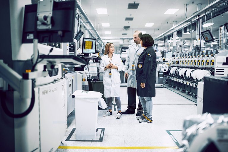 Drei Menschen in Kitteln stehen in einem Labor