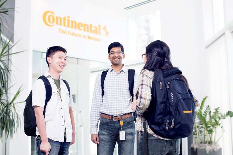 Two young men and a young woman wearing casual business attire standing in a lobby and talking to each other in front of an elevator 