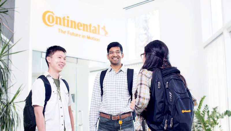 Two young men and a young woman wearing casual business attire standing in a lobby and talking to each other in front of an elevator