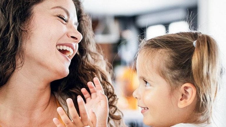 Eine junge Mutter hält ihre Tochter auf dem Arm und beide lächeln.