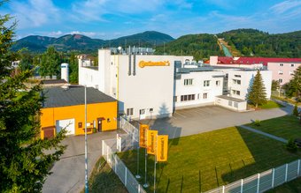 Pohled z dronu na bíložluté budovy areálu Continental ve Frenštátu pod Radhoštěm se zelenými kopci v pozadí