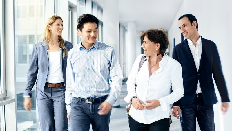 Zwei Frauen und zwei Männer in Businesskleidung gehen lächelnd einen Flur hinunter