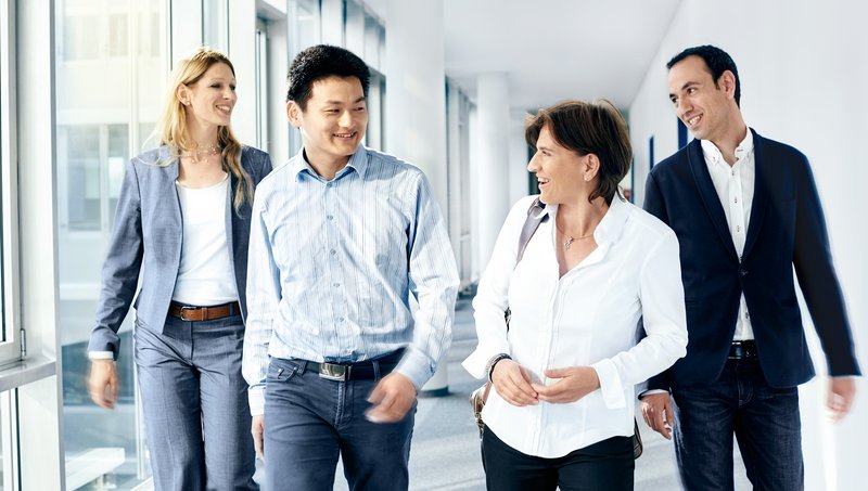 Two men and two women in business outfits walk down a hallway smiling