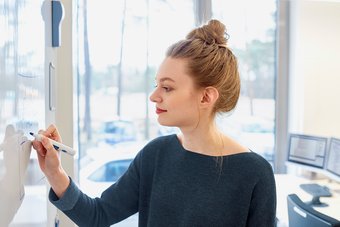 a young woman with red hair and red lipstick stands in front of a white board and writes something on it