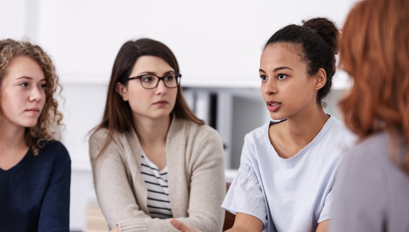 Vier junge Frauen sitzen in einem Kreis und schauen sich konzentriert an