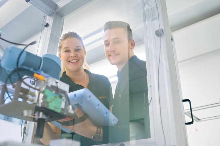 Eine junge Frau und ein junger Mann schauen in eine mit Plexiglas verkleidete Maschine