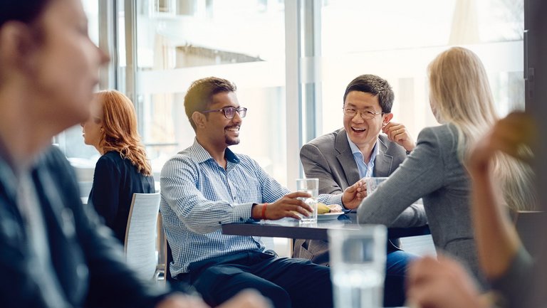Two men sit with a woman at a table in a canteen and laugh