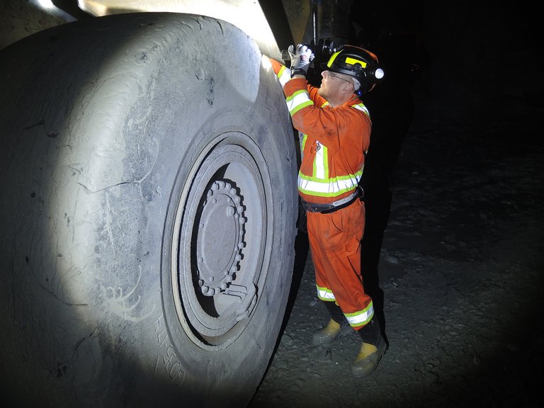 A man in safety clothes is checking a giant tire in the dark with a flashlight