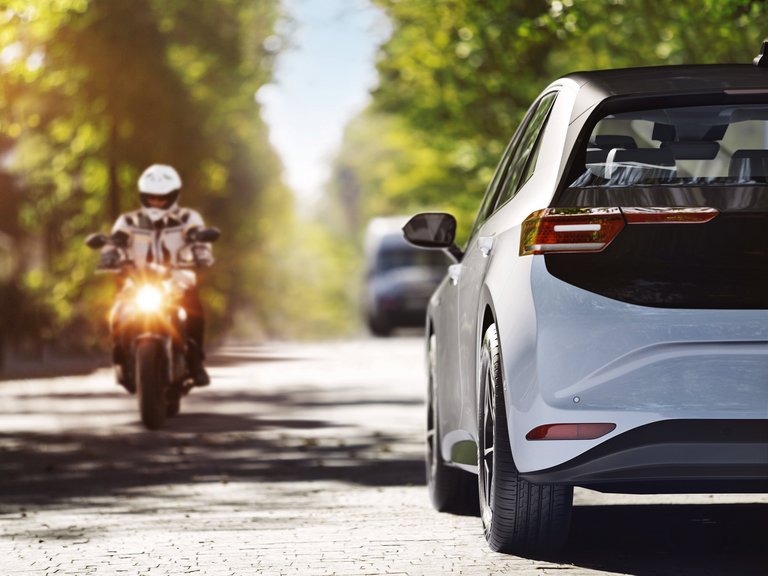 A car and a motorcycle travel along a street with trees