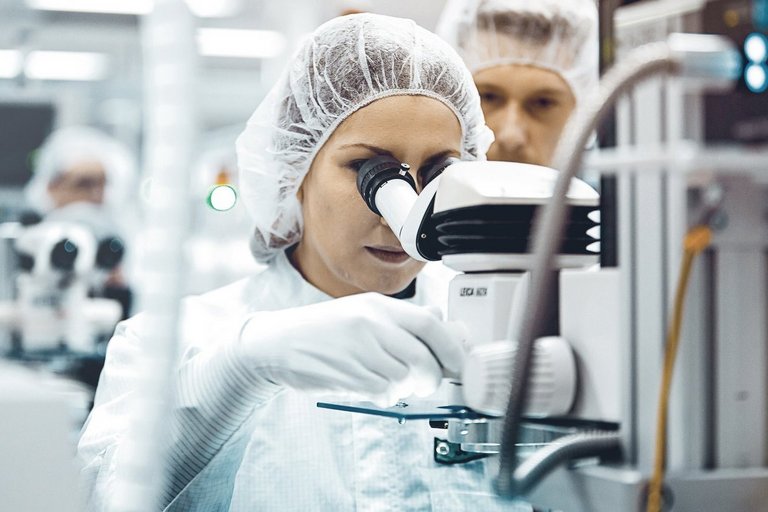 Eine Frau im weißen Kittel mit Haube schaut in ein Mikroskop