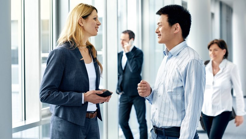 Zwei Männer und zwei Frauen in Business-Outfits gehen lächelnd einen Flur hinunter