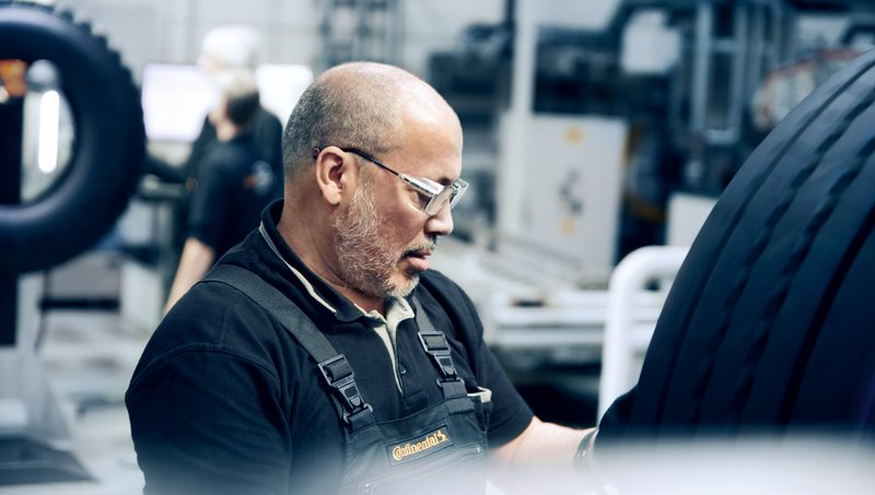 Older man with three-day beard in dungarees checks a tire