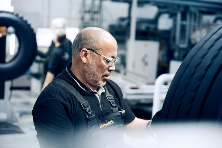 Older man with three-day beard in dungarees checks a tire