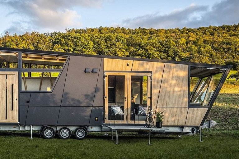 Ein futuristisches Tiny-House steht auf einer Wiese vor einer Waldböschung