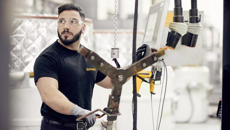 A young man with safety goggles operates a machine in a production surrounding