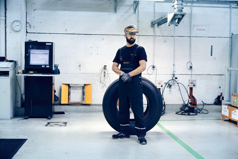 Ein Mann mit Schutzbrille steht in einer Prüfhalle vor einem großen Reifen
