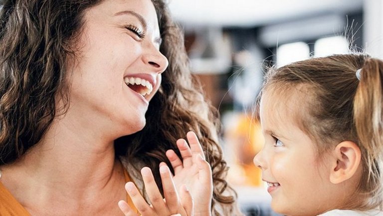A young mother holds her daughter in her arms and they both smile.